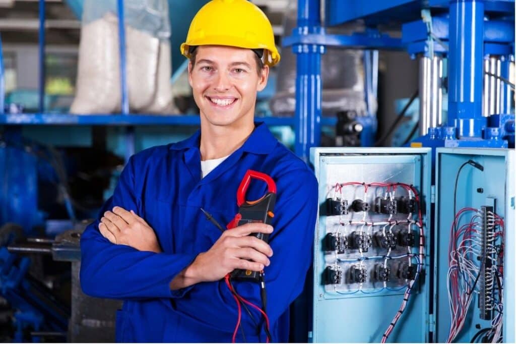Smiling Electrician With Clamp Meter And Open Panel